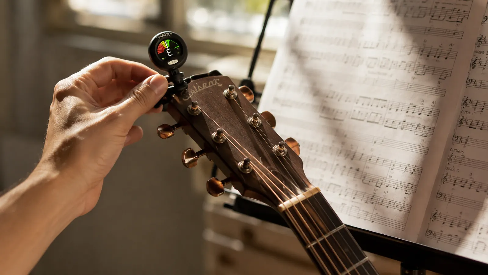A hand clipping a small clip-on tuner onto the headstock of an acoustic guitar in a sunlit practice room